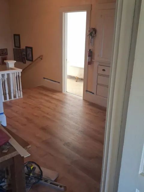 Warm wood-look planks run through the room toward a bright doorway, with white trim at the edges.