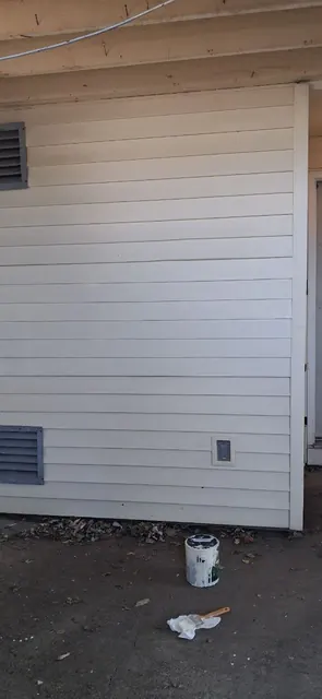 Light-colored horizontal siding fills the wall, with a paint can and supplies at ground level.