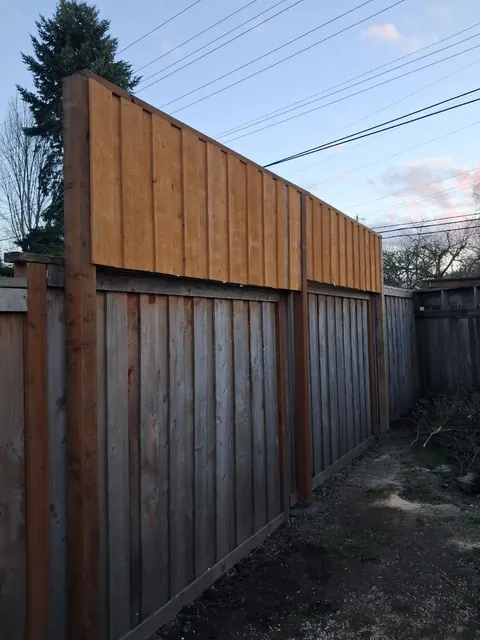 A row of taller warm-toned boards rises above an older weathered fence section.