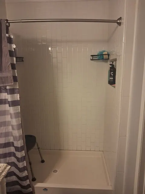A light tile shower enclosure with a curtain rail, corner baskets and a recessed shelf.