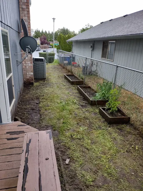 The side passage is open again, revealing three raised planting beds along the chain-link fence.
