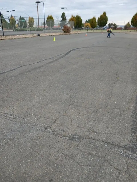 A broad asphalt parking area with cones and people in the distance during site work.
