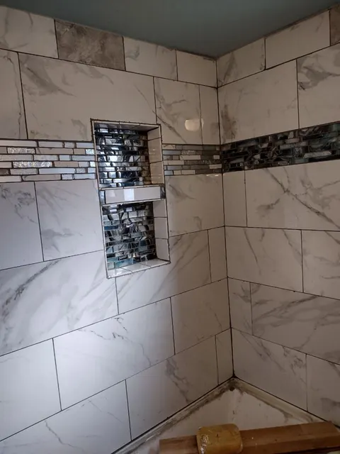 Marble-look wall tiles surround two stacked mosaic niches. The tub edge and tools show this is still a work site.
