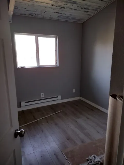 A doorway view shows the gray room, contrasting white trim and plank floor while cleanup is still underway.