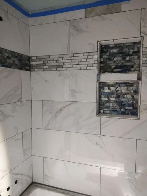 A horizontal mosaic accent runs into the stacked niches above the tub. Masking tape remains along the ceiling edge.