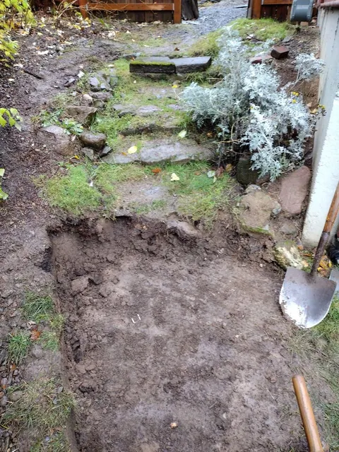 Grass and soil cover parts of the existing steps, while a dug-out lower section and shovel show work underway.
