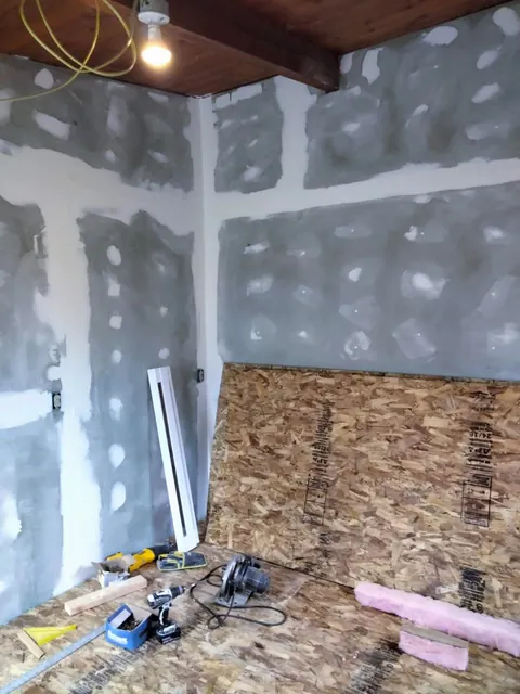 Drywall panels have taped and coated seams, while tools and materials remain on the unfinished floor.